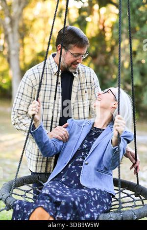 Happy mature couple enjoying a swing in a sunny outdoor park. Stock Photo