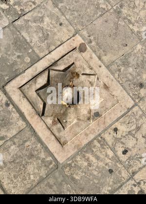 Carved stone paver with an eight-pointed star design on a floor. Stock Photo