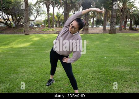 Woman doing side stretch exercise outdoors in a park Stock Photo