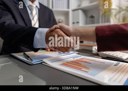 A business agreement moment captured as two professionals shake hands over financial reports, representing collaboration, partnership, and successful Stock Photo
