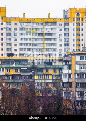Residential buildings with multiple rows of windows and balconies showing brutalist yellow and gray facade architecture, standing behind leafless tree Stock Photo