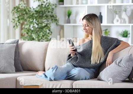 Blonde woman using cell phone sitting on a couch at home Stock Photo