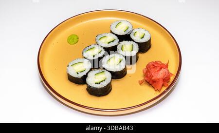 Traditional cucumber hosomaki sushi rolls served with wasabi and pickled ginger on yellow ceramic plate isolated on white background. Stock Photo