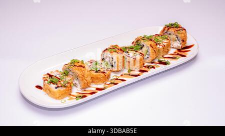 Deep fried sushi rolls with avocado, spring onions and sauce drizzle served on white ceramic plate isolated on white background. Stock Photo