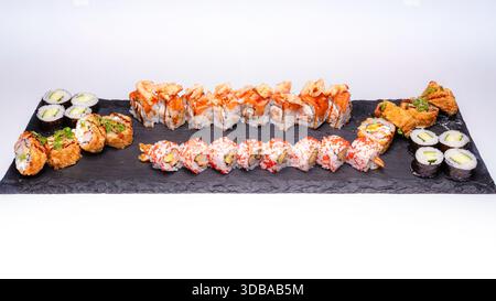 Assorted sushi platter with various sushi rolls and maki served on black slate board isolated on white background. Stock Photo