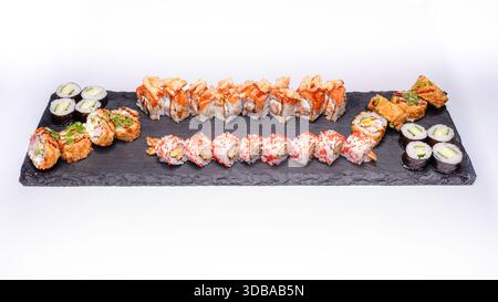 Large mixed sushi platter with uramaki, maki and fried sushi rolls served on black slate board isolated on white background. Stock Photo