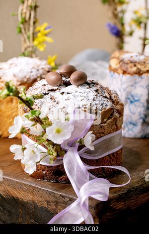 Homemade Italian traditional Easter panettone cake, decorated by chocolate eggs, pink ribbon and blossoming cherry tree flowers standing on wooden tab Stock Photo