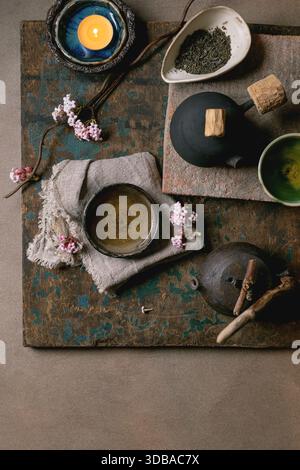 Chinese Tea Ceremony. Two traditional handmade ceramic black teapot with wooden handle on dark wooden table. Ceramic teacups and pink spring flowers, Stock Photo