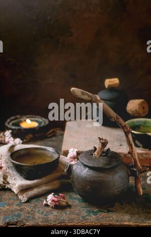 Chinese Tea Ceremony. Two traditional handmade ceramic black teapot with wooden handle on dark wooden table. Ceramic teacups and pink spring flowers, Stock Photo