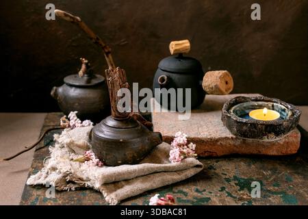 Chinese Tea Ceremony. Three traditional handmade ceramic black teapots with wooden handle on dark wooden table. Ceramic teacups and pink spring flower Stock Photo