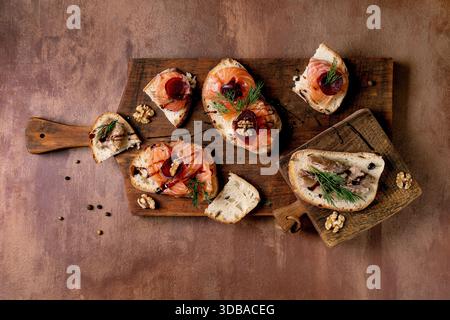 Sandwiches with thinly sliced salted salmon fillet, sardines, beetroot slices, walnuts, balsamic vinegar and fresh wheat bread on wooden board. Brown Stock Photo