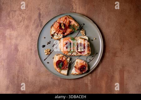 Sandwiches with thinly sliced salted salmon fillet, beetroot slices, walnuts, balsamic vinegar and fresh wheat bread on grey plate, fine dining. Brown Stock Photo