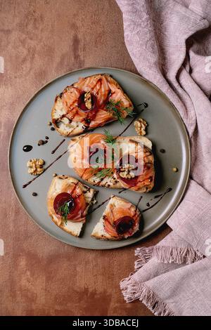 Sandwiches with thinly sliced salted salmon fillet, beetroot slices, walnuts, balsamic vinegar and fresh wheat bread on grey plate, fine dining. Brown Stock Photo