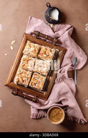 Homemade Norwegian sweet cake Verdens Beste Kake with custard, meringue, and almonds, cut into squares, served on wooden tray. Beige background, pink Stock Photo