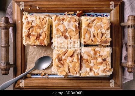 Homemade Norwegian Verdens Beste Kake with custard, meringue, and almonds, cut into squares, served on wooden tray with spoon. Top view, close-up. Stock Photo