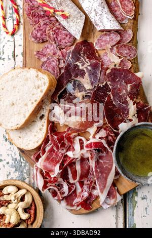 Snack board with traditional Spanish ham Jamon Iberico, sliced Fuet sausage, green olives, white bread, nuts, olive oil. Light rustic wooden backgroun Stock Photo