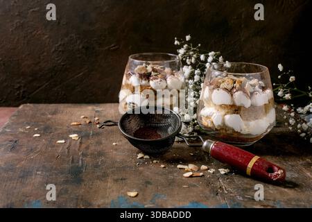 Classic Italian tiramisu in two glasses. Layers of sponge cake and mascarpone cream with cocoa powder. Placed on rustic wooden table with vintage siev Stock Photo