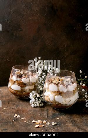 Classic Italian tiramisu in two glasses. Layers of sponge cake and mascarpone cream, dusted with cocoa powder. Placed on rustic wooden table. White ba Stock Photo