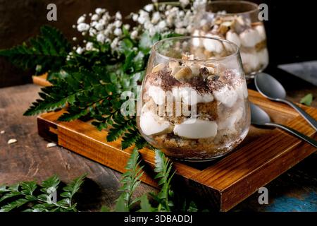 Classic Italian tiramisu layered dessert with cocoa powder and almonds in two glasses. Served on tray with spoons on old wooden table. Decorated white Stock Photo