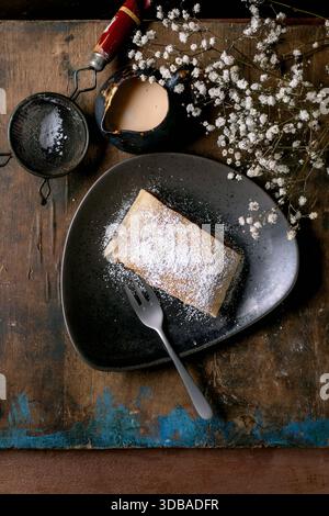 Traditional Austrian homemade pastry apple strudel with raisins. Slice on ceramic plate, dusted with powdered sugar. Old wooden table, small jug with Stock Photo