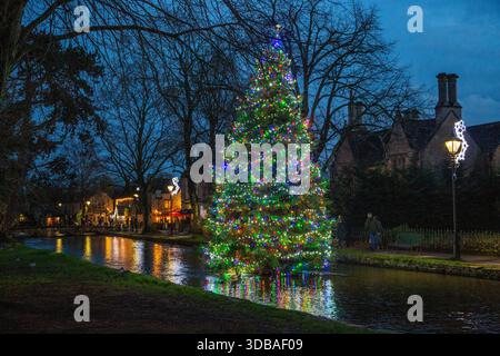 Floating decorated christmas  tree with lights, on the river Windrush as it passes through the Cotswold village of Bourton on the Water Gloucestershire Stock Photo