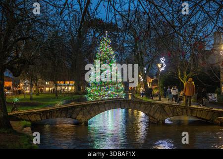 Floating decorated christmas  tree with lights, on the river Windrush as it passes through the Cotswold village of Bourton on the Water Gloucestershire Stock Photo