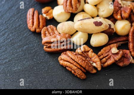 Mixed nuts including pecans and macadamia nuts on dark stone surface. Healthy snack concept, close up Stock Photo