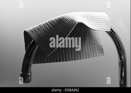 A minimalist black-and-white still life showing a textured cleaning cloth draped over a curved chrome bar, emphasizing fabric detail, soft shadows, an Stock Photo