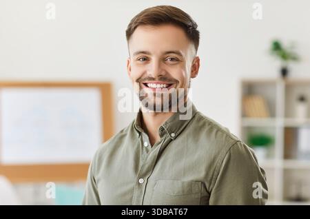 Portrait of confident young bearded handsome business man looking cheerful at camera in office. Stock Photo