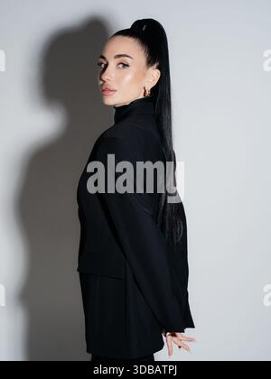 Elegant young woman black blazer high long ponytail looking back over shoulder. Confident businesswoman portrait studio shot. Fashion style power beau Stock Photo