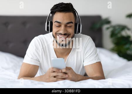 Happy Young Man Enjoys Technology While Relaxing in Bed With Smartphone Stock Photo
