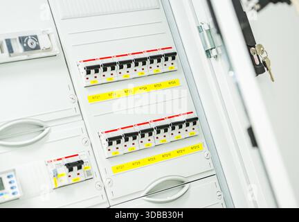 Circuit breakers are arranged on a control panel inside an electrical room. The panel shows various labels and keys. Stock Photo