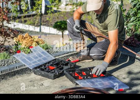 A person is working on Building Irrigation System in a garden with tools laid out in containers. The sun is shining on the scene. Stock Photo
