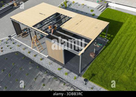 Two workers are installing a roof on a new structure in a backyard. They are using tools and materials. Stock Photo