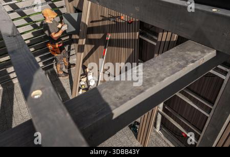 A worker stands on a framework putting up panels on a building under construction while tools are arranged nearby. Stock Photo