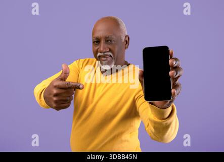 Senior Man Shows Smartphone and Smiles at the Camera in Indoor Setting With Violet Background Stock Photo