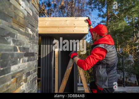 A person is on a ladder, adding wood to a structure near a home. Stock Photo