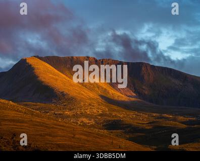 View of golden sunlight bathing the rugged mountain range under a soft, cloudy sky, creating a serene yet dramatic landscape, Loch Morlich, Cairngorm Stock Photo