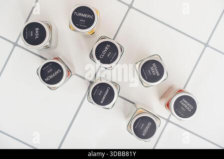 Assorted spices in glass jars with metal lids on the tile kitchen counter top view Stock Photo
