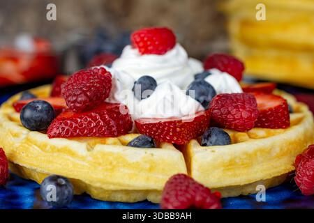 An extreme close-up highlights the fresh raspberries, blueberries, and sliced strawberries with whipped cream on a golden waffle in Waukesha County. Stock Photo