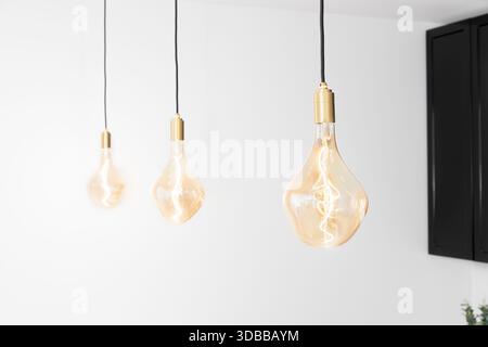 Three vintage Edison style light bulbs with a warm amber glow hang from the ceiling in a modern minimalist interior Stock Photo