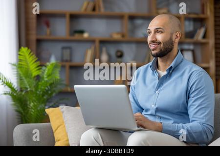 Happy young entrepreneur using a laptop, enjoying flexible remote work from the comfort of his modern home office setup, achieving work-life balance and career success Stock Photo