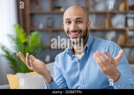 Friendly bald bearded man smiling and animatedly gesturing while speaking during a virtual meeting or video call from home, confident and engaging communicator Stock Photo