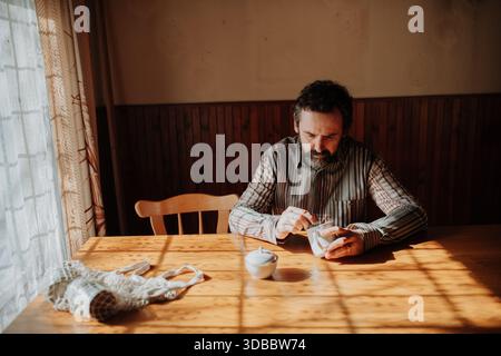Portrait of poor despaired man sitting at table drinking tea. Stock Photo