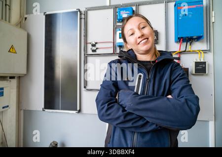 Female technician standing with arms crossed next to renewable energy electrical equipment Stock Photo