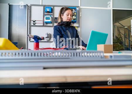 Woman engineer monitoring solar power control panel with laptop in a workshop setting Stock Photo