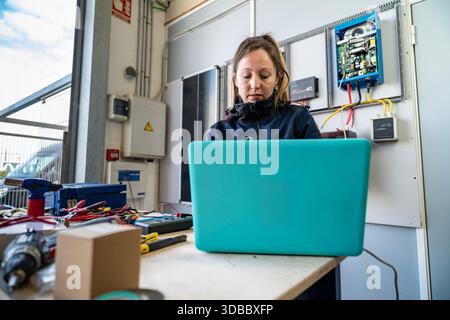 Female technician troubleshooting solar inverter system using a laptop in workshop Stock Photo