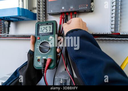 Hands using a digital multimeter to test voltage on a solar charge controller Stock Photo