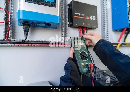 Hands using a multimeter to test electrical current on a solar charge controller Stock Photo