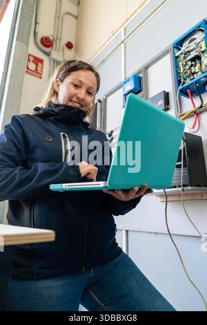 Woman engineer smiling while working with a laptop on a renewable energy control panel Stock Photo